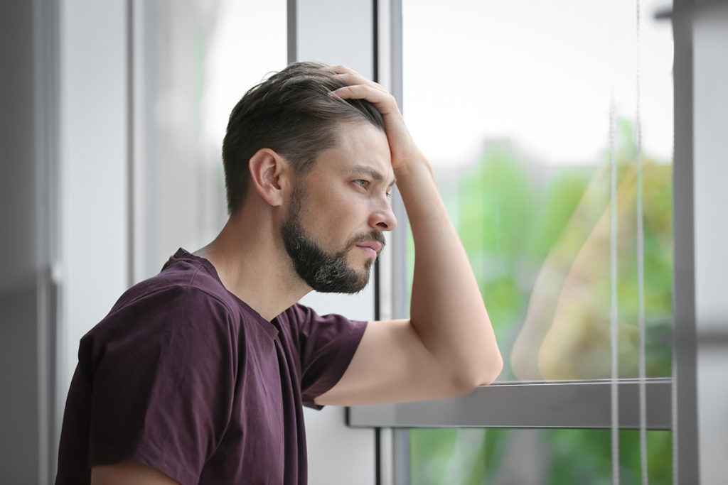 man looks out window with his hand in his hair struggling with signs of codeine addiction