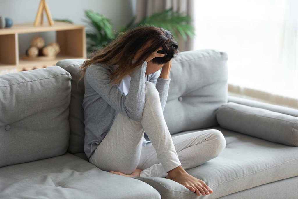 a woman on the couch struggling and showing Signs of Anxiety