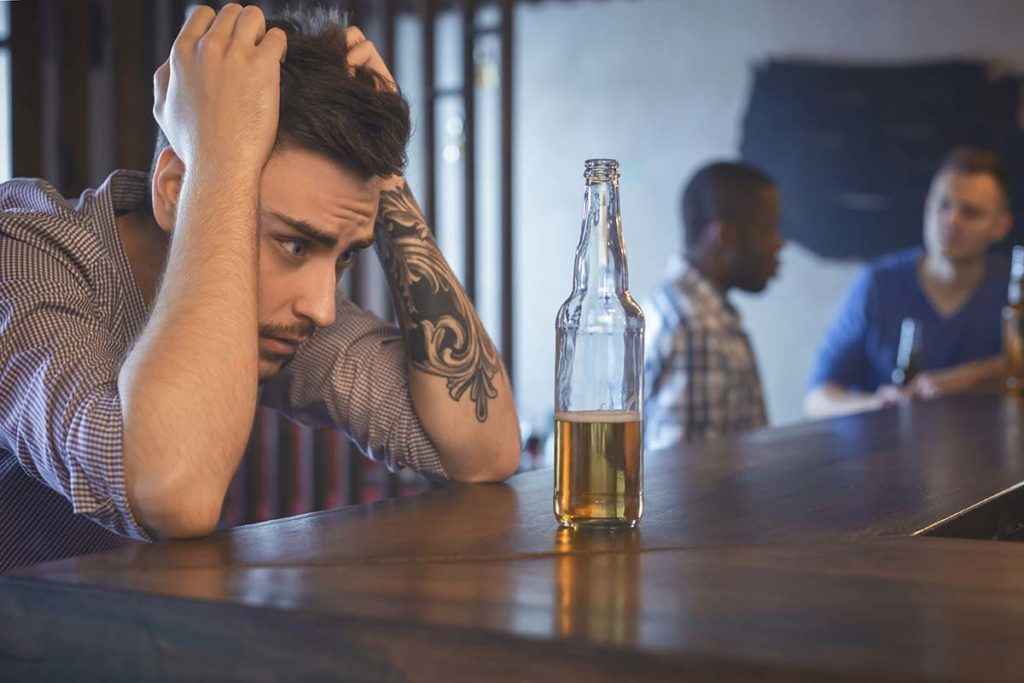 a man staring at a drink wondering Am i an Alcoholic?