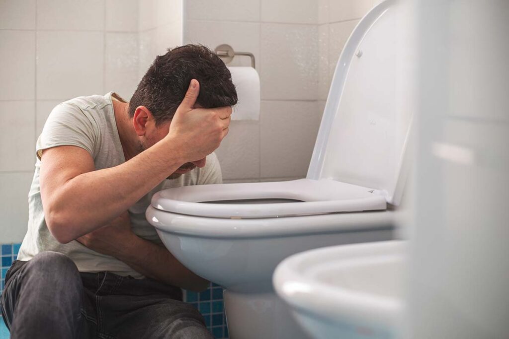 a person holds their head beside a toilet dealing with the dangers of binge drinking