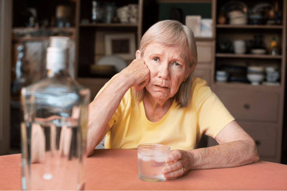 Elderly woman with a glass of vodka showing her drinking problem and alcohol abuse