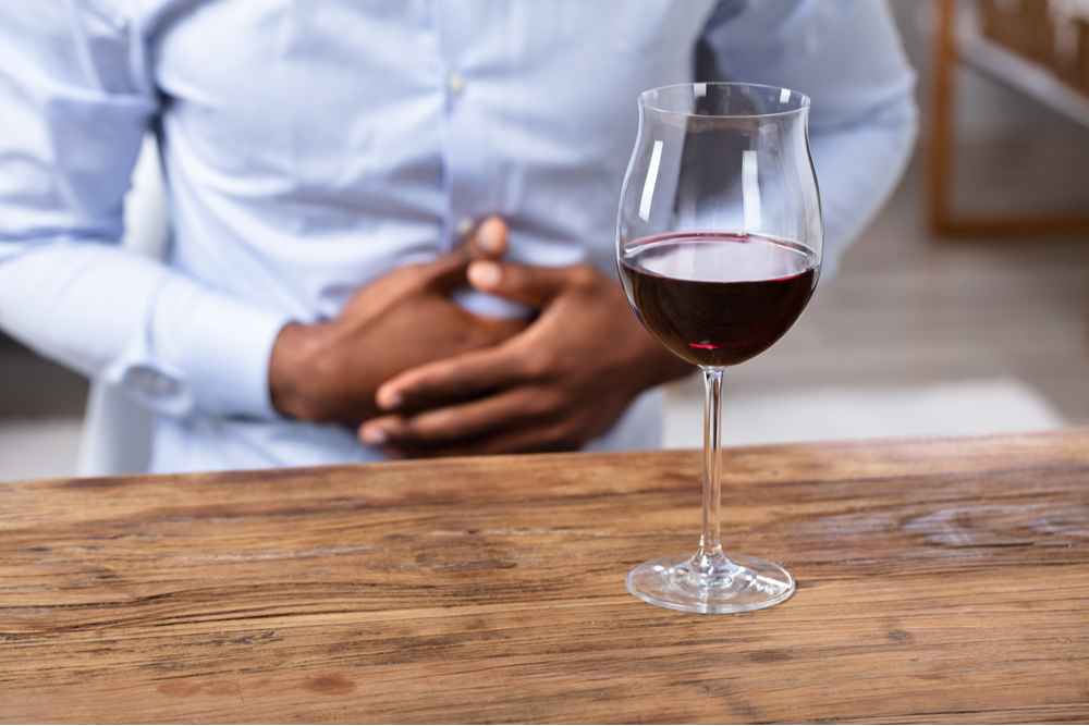 Man clutching stomach with wine of the table, emphasizes effects of Alcohol on gut health and importance of gut health