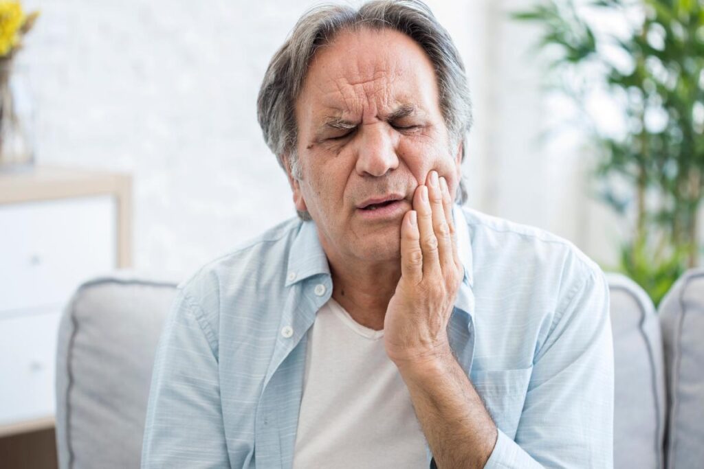 a person sits and rubs their jaw in pain possibly feeling the link between drugs and oral health