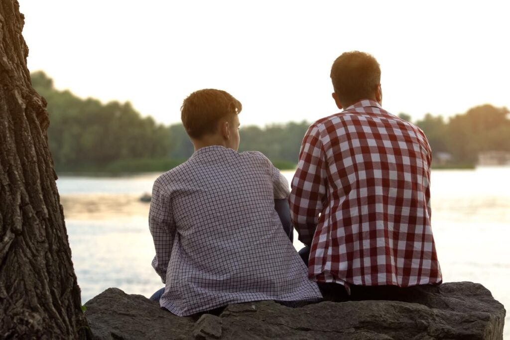 father and son sitting on log talking about whether alcoholism is hereditary