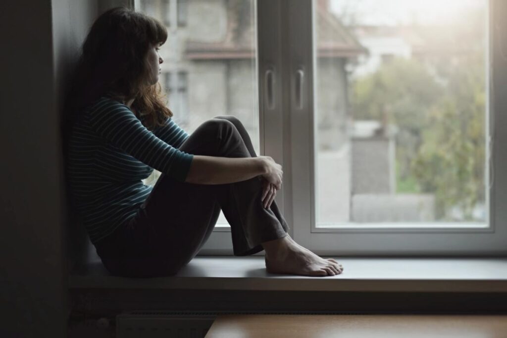 a person sits in a windowsill dealing with the Signs of Adderall Addiction