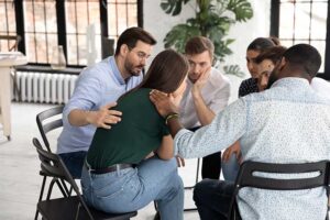 a group of people comforts a person with long hair as they all sit in a circle in chairs at a heroin detox center