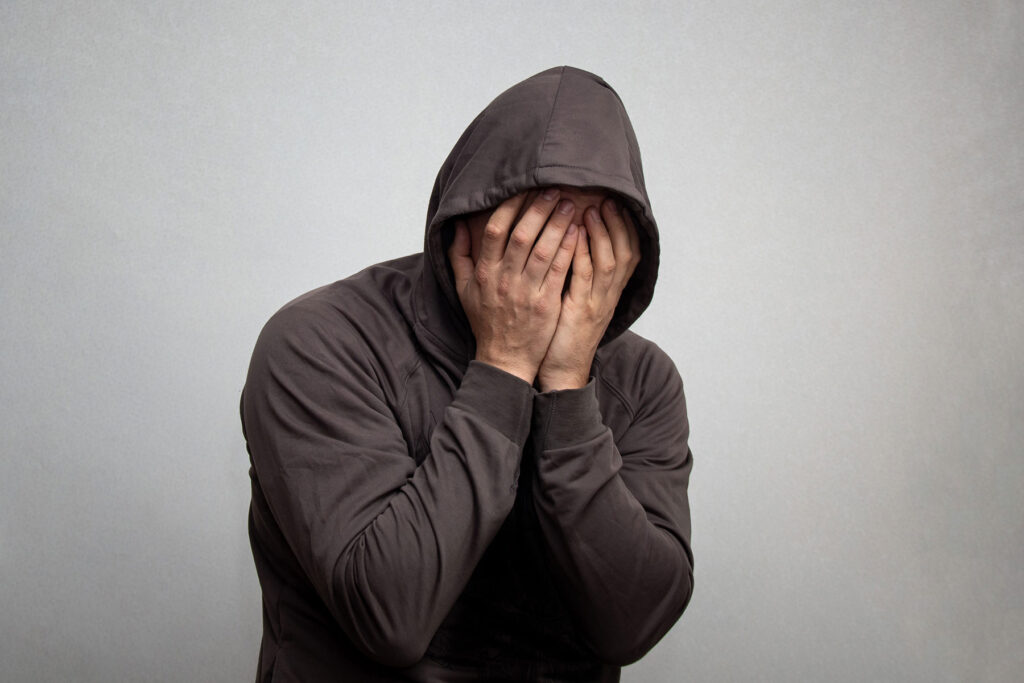 a person puts their face in their hands while wearing a hoodie showing signs of meth withdrawal