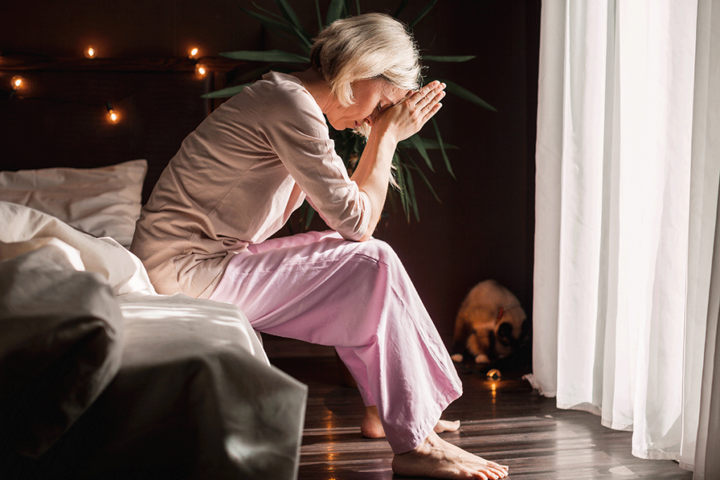 an upset woman sits on the edge of her bed resting her head on her hands showing effects of repressed trauma