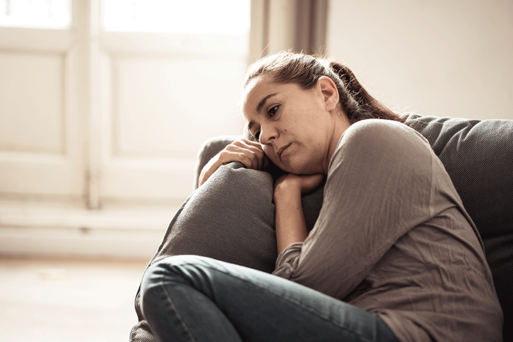 a sad woman sits on her couch curled up with a pillow displaying some signs of depression