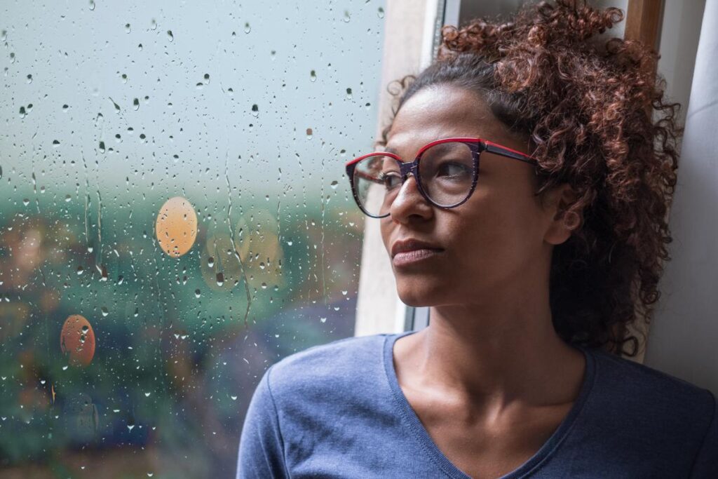 woman with glasses leans against her window and looks out wondering about the link between sad and addiction