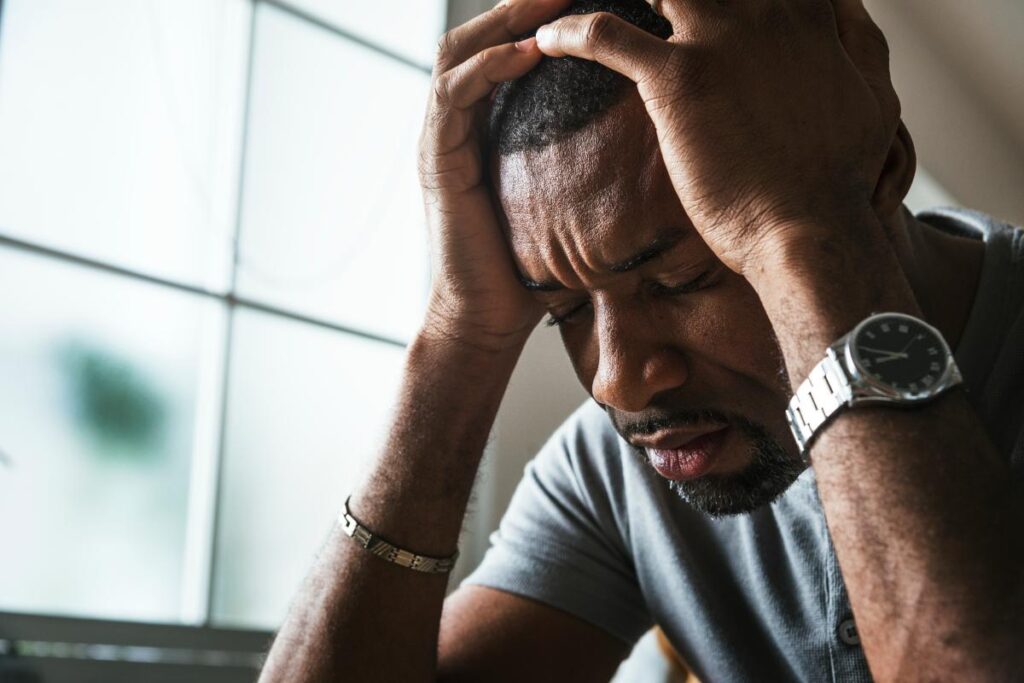 distraught man leans his head on his palms struggling with alcohol and falling down