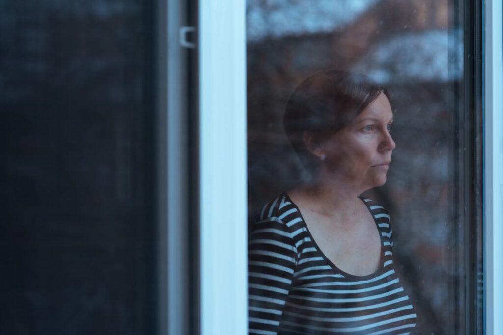 woman looks out her window looking solemn and wondering about the dangers of opioid use during winter