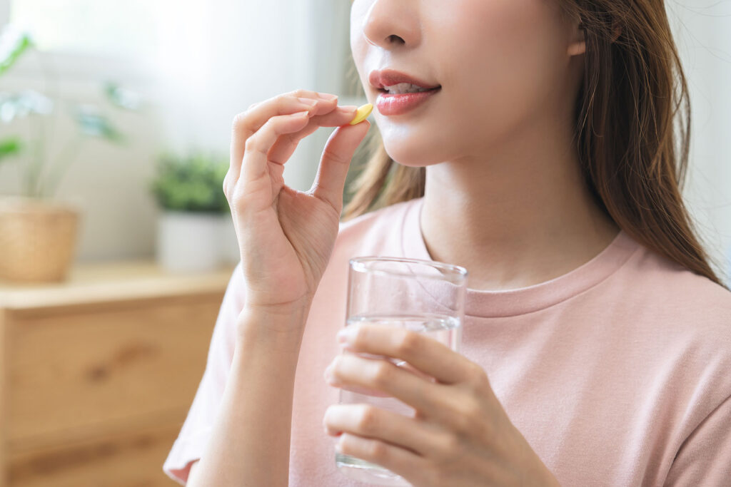 woman holds pill to mouth in one hand and the other holds a glass of water while she wonders what is 2C-B?