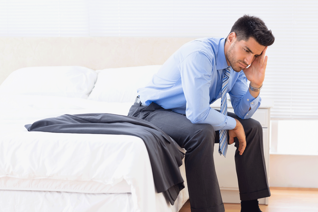 man in a suit sits on the edge of his bed holding his head in his hand and wondering is subutex addictive