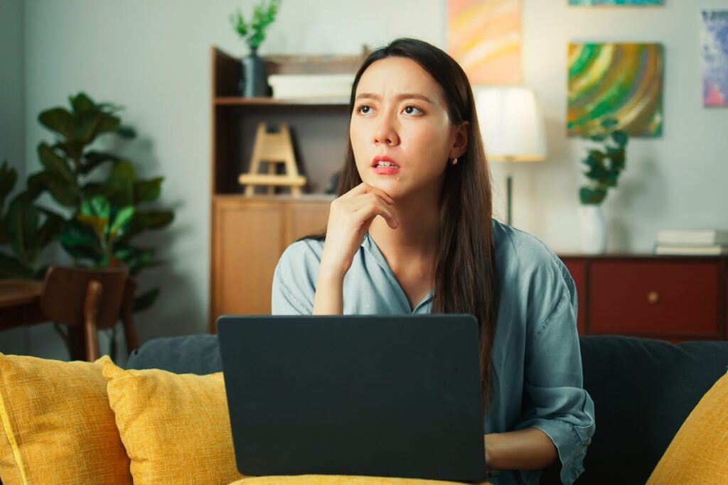 woman sits on her couch with her laptop in front of her and looks up and wonders what is the difference between thc and cbd