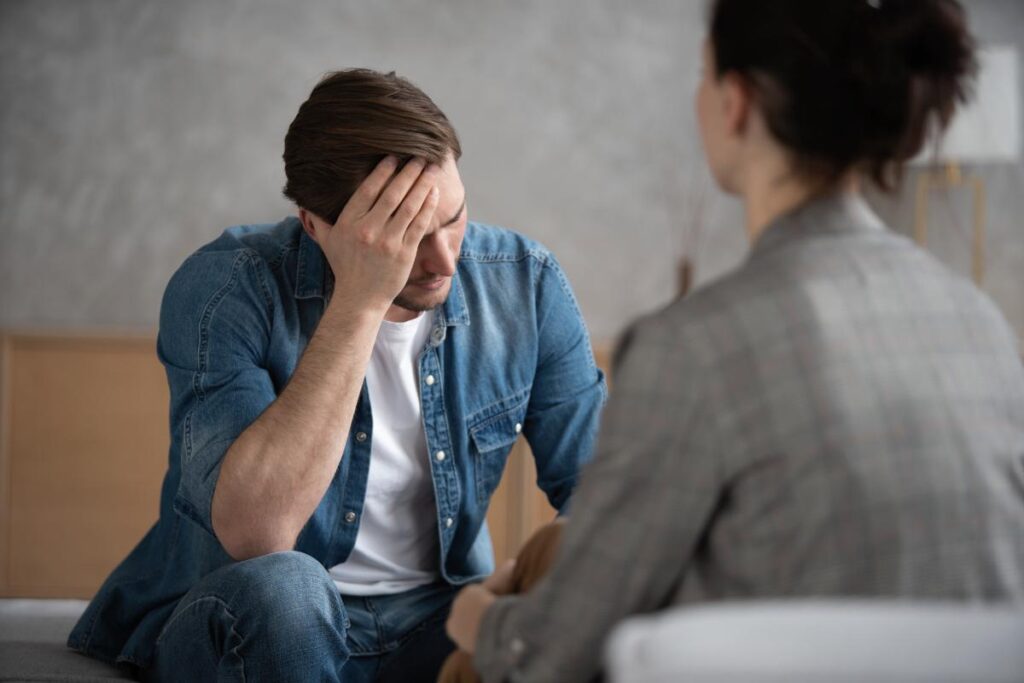 upset man sits on a couch holding his hand to his forehead asking his therapist what is angel dust slang for