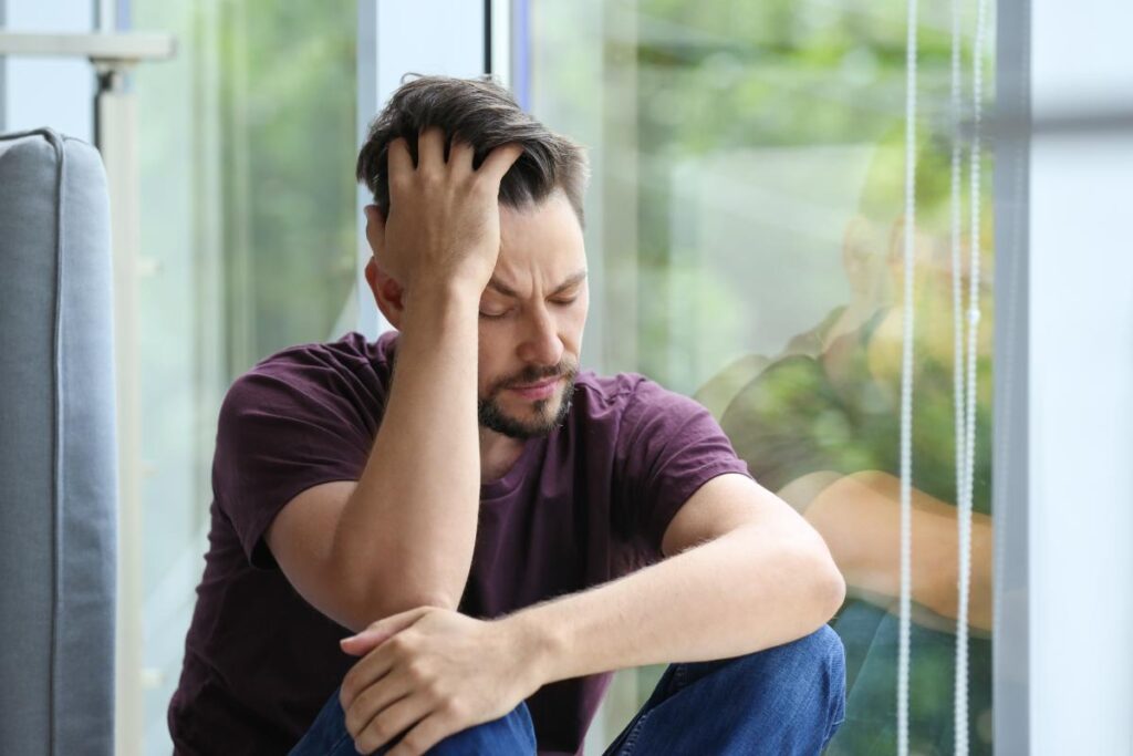 person sitting near window looking distressed struggling with headache as one of many long term effects of heroin