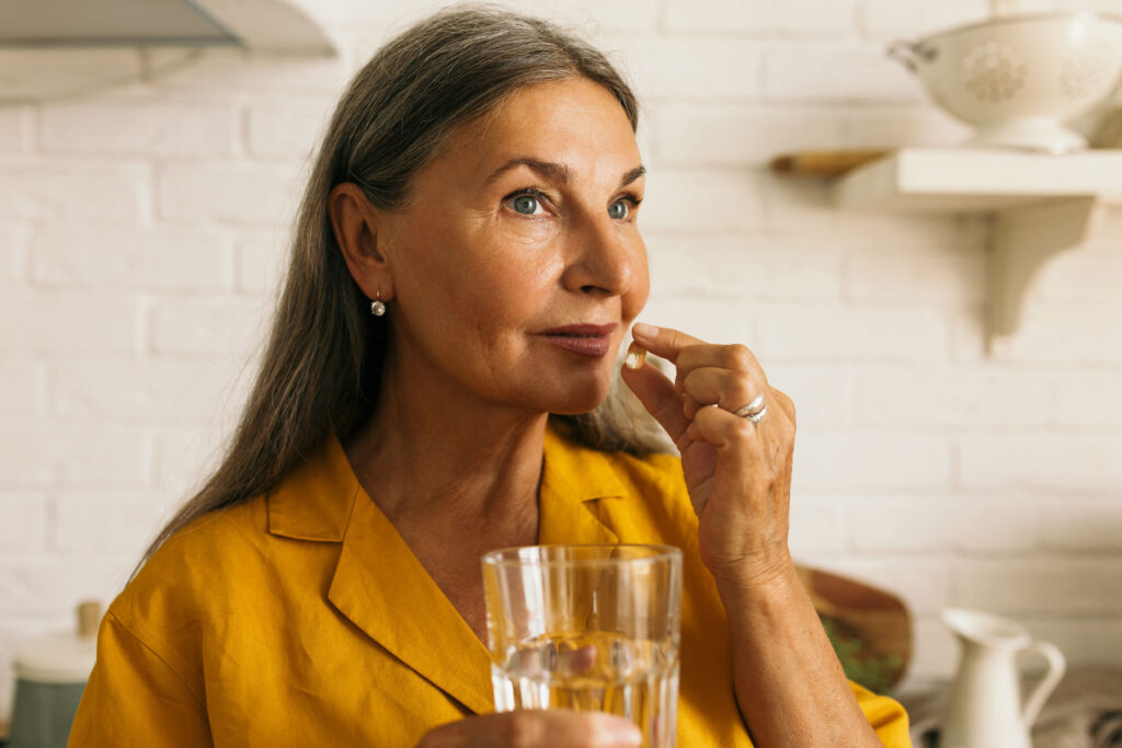 A woman stands in her kitchen with a glass of water and an Ambien pill in her hand. She is addicted to Ambien.